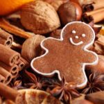 A smiling gingerbread cookie surrounded by cinnamon sticks, star anise, dried citrus fruit slices, and other holiday spices.